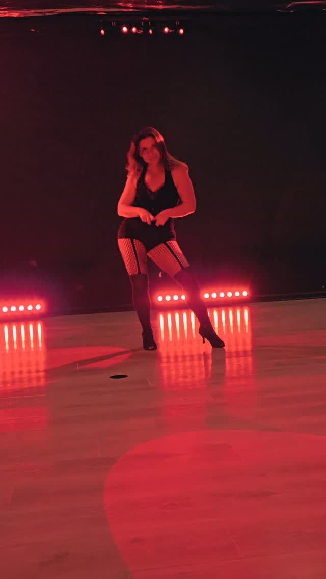 A dancer in fishnets and heels mid-move under red floor lights